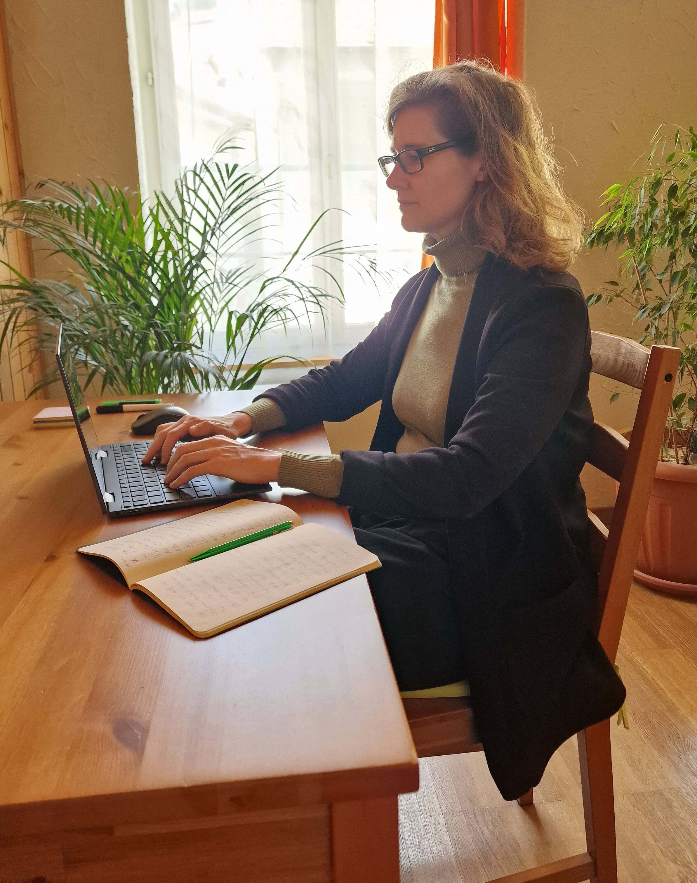 Silvana Huber sitzt an einem Holztisch und schreibt auf einem Laptop.